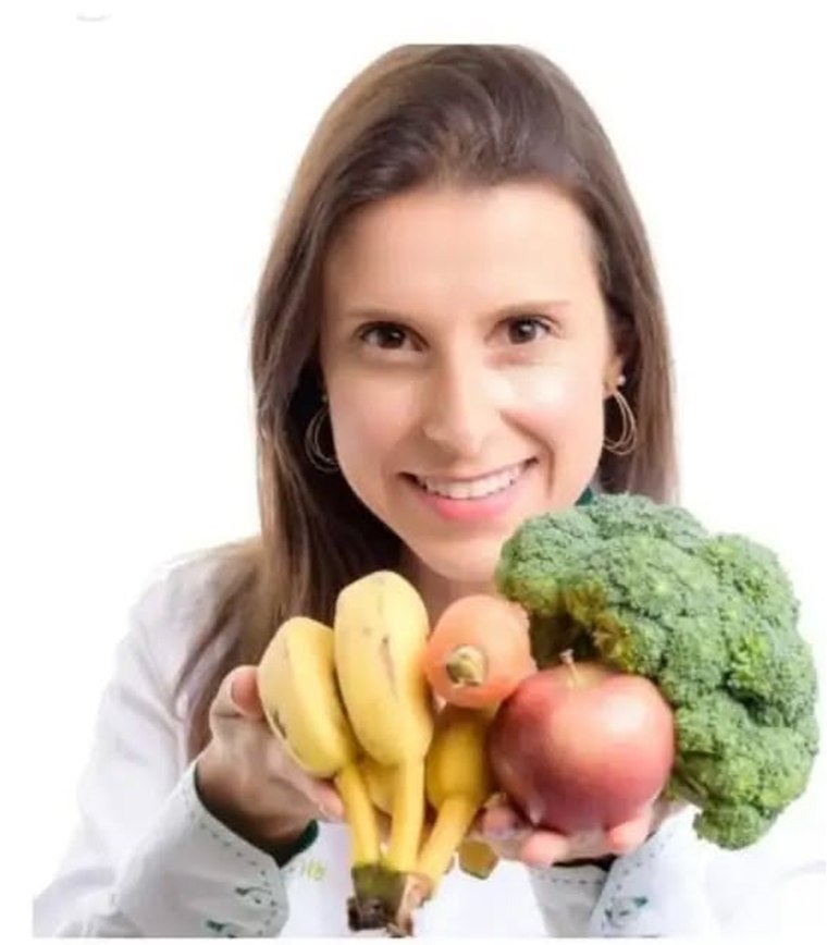 Sabrina Ribes Zibetti, nutricionista, de jaleco branco, segurando frutas e legumes